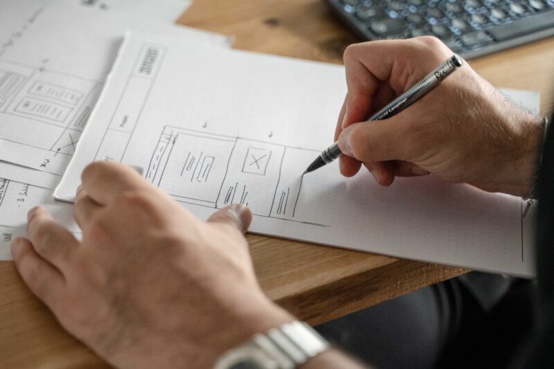 Eine Person, die mit einem Stift auf ein Blatt Papier schreibt und dabei den Schwerpunkt auf Webdesign legt.