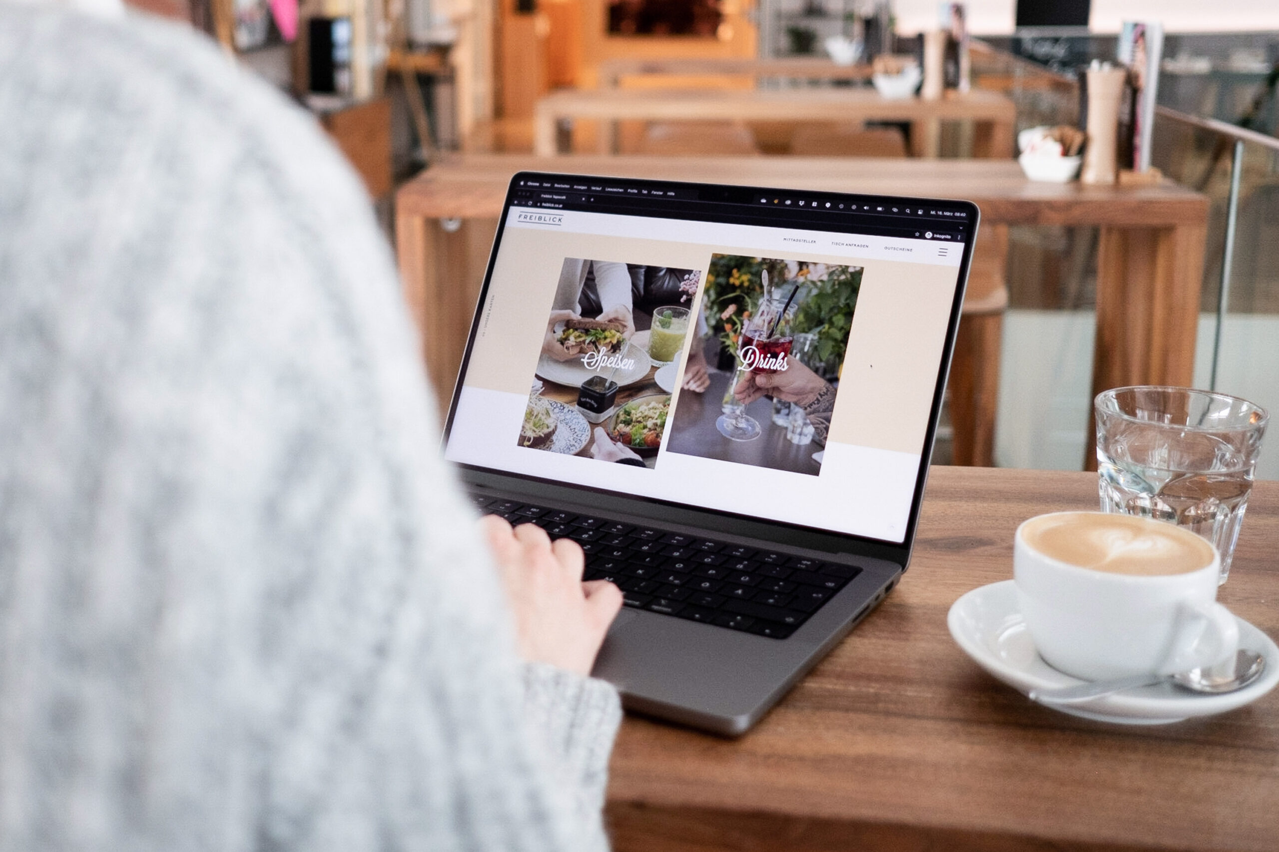 A woman enjoying Freiblick at a café while using a laptop and sipping coffee.