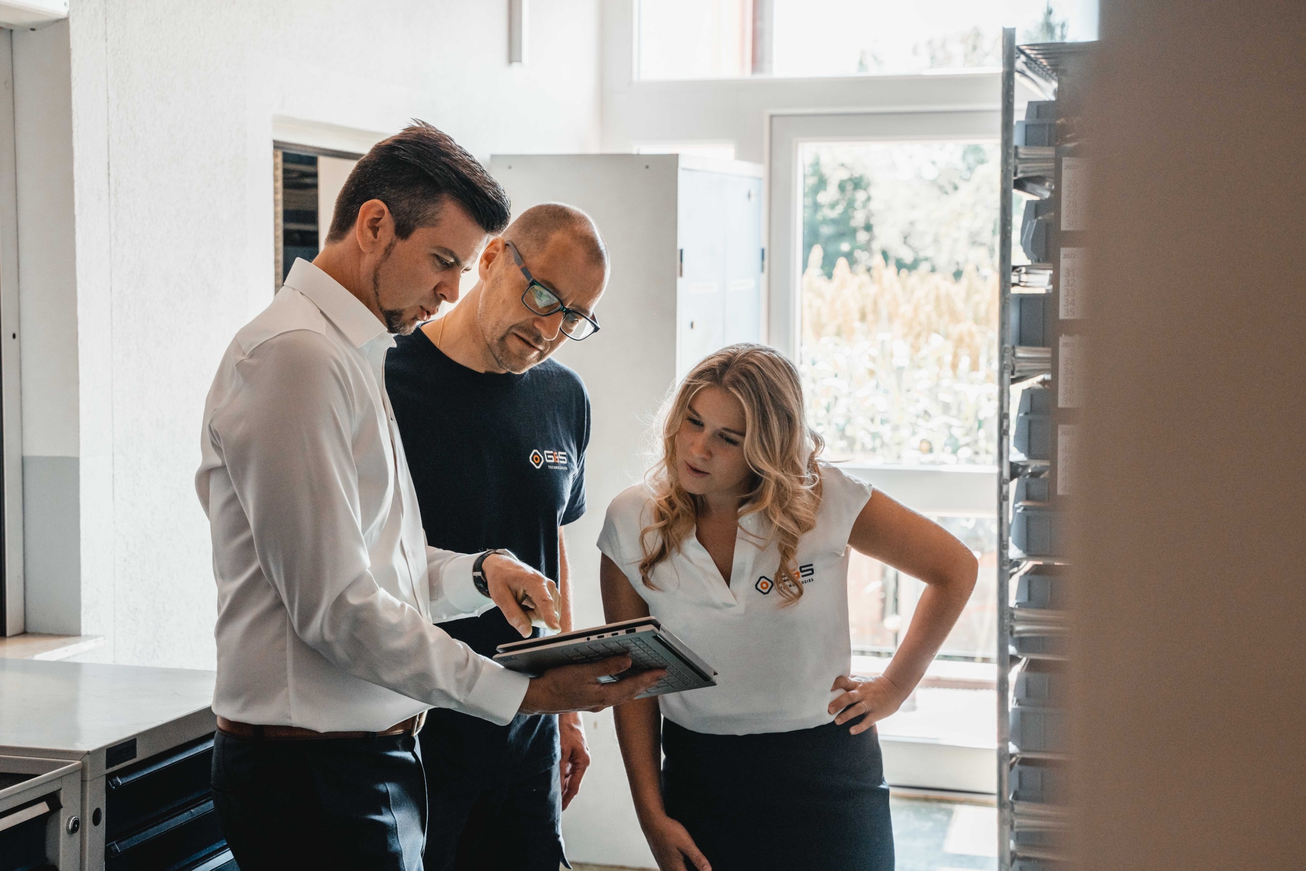 Drei Personen bei G&S Technologies stehen in einer Küche und schauen auf ein Tablet.