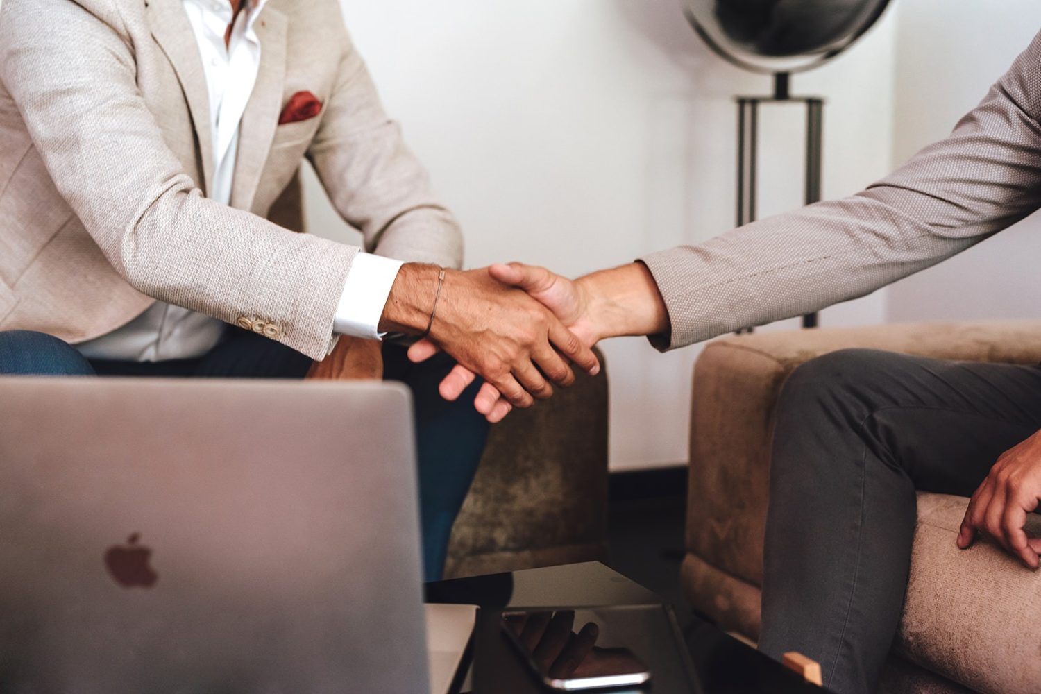 Two businessmen shaking hands in front of a laptop, showcasing Valere.