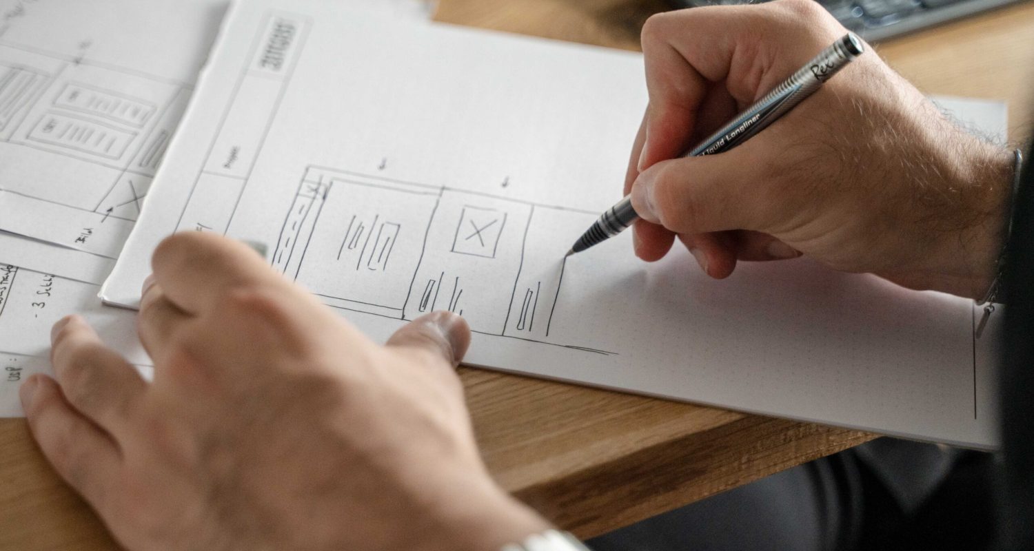 Eine Person, die mit einem Stift auf ein Blatt Papier schreibt und dabei den Schwerpunkt auf Webdesign legt.