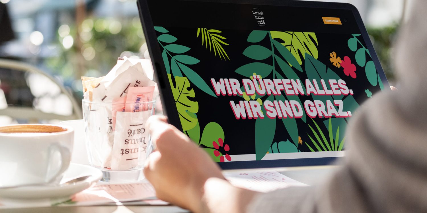 Eine Person sitzt mit einem Laptop und einer Tasse Kaffee an einem Tisch im Kunsthauscafé.